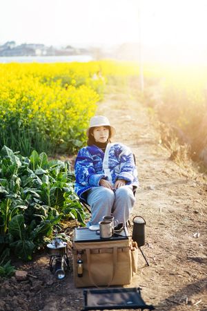 一个戴帽子的小姐坐在黄花的田野里的一只箱子上