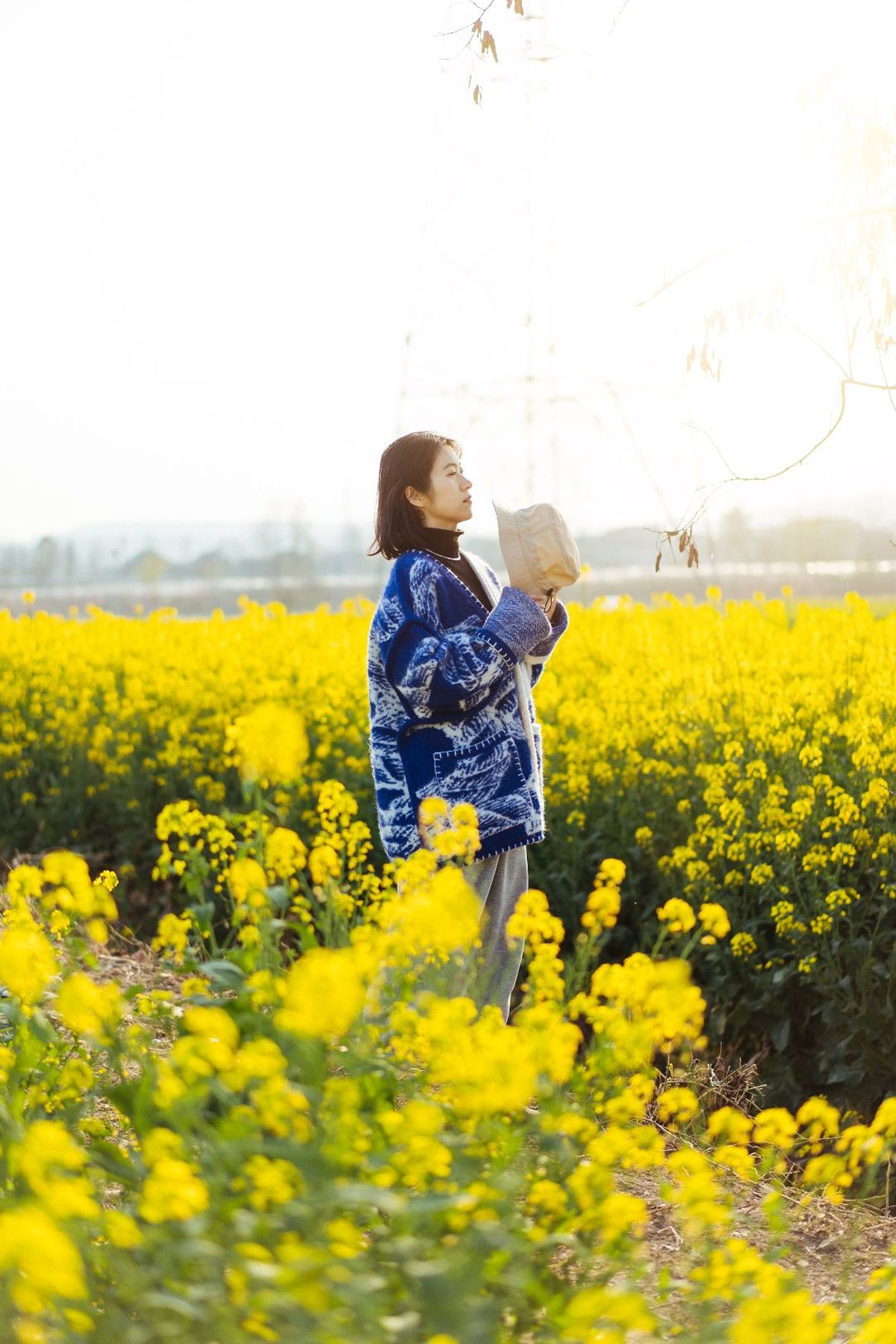 一位年轻女子站在一片黄花的田野中