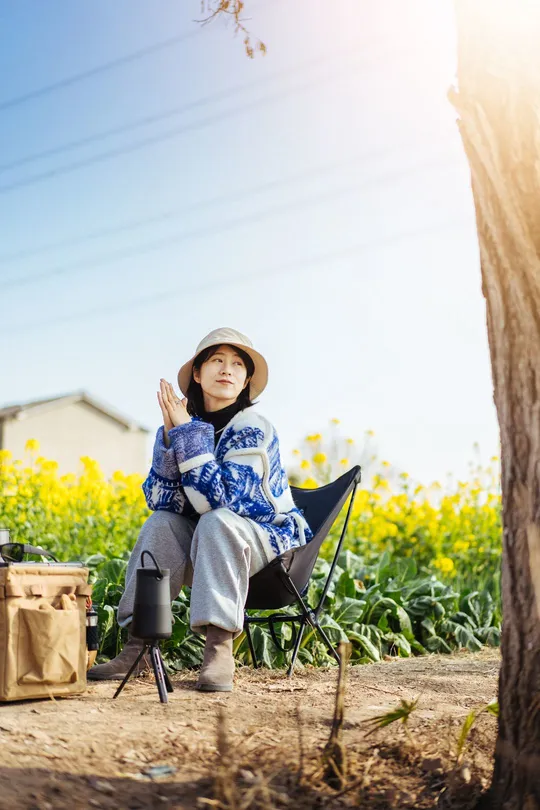 一位妇女坐在树下草地上的椅子上