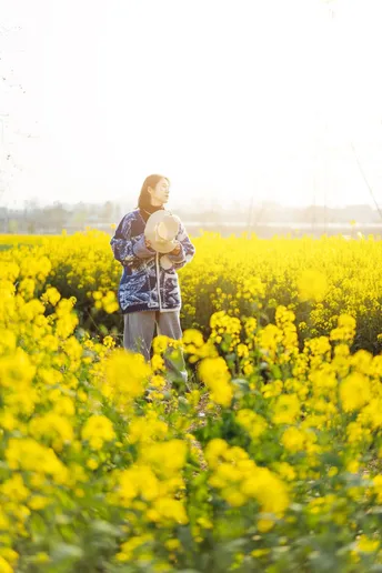 一位戴帽子的女士站在一片黄花的田野中