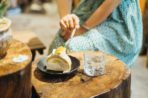 一个坐在木制桌子上的女人 盘子里放着食物 叉子切着一块蛋糕。