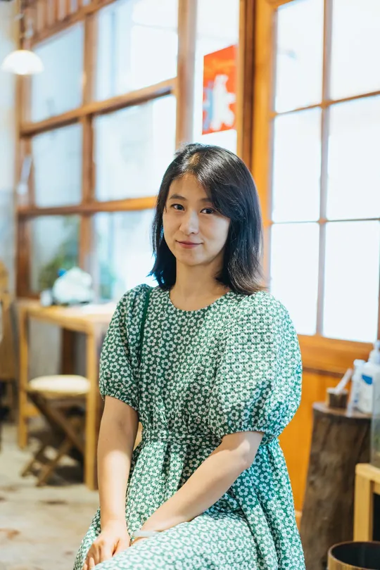 一个穿着绿色连衣裙的年轻女子坐在一个有桌子和椅子的房间里