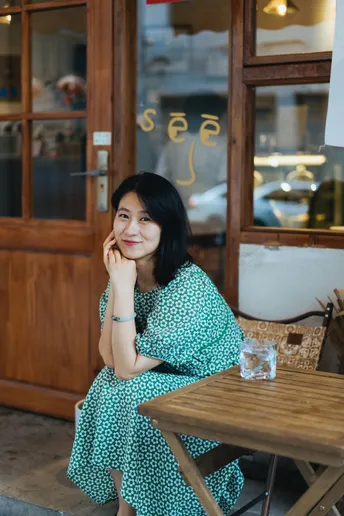 一位穿着绿色连衣裙的年轻女子坐在咖啡馆的桌子旁 微笑着。