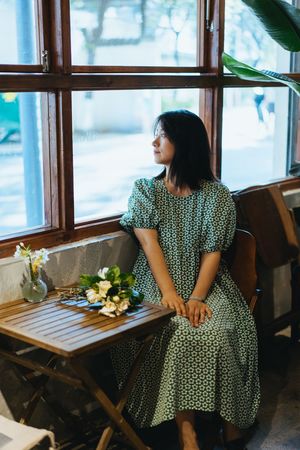 一个穿着连衣裙的年轻女子坐在咖啡馆的桌子旁 凝视着窗外。