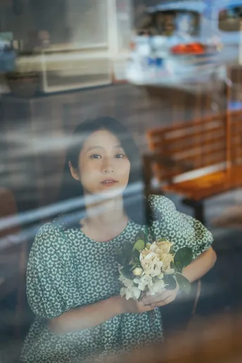 一个穿着连衣裙的小女孩抱着一束花 凝视着窗户。