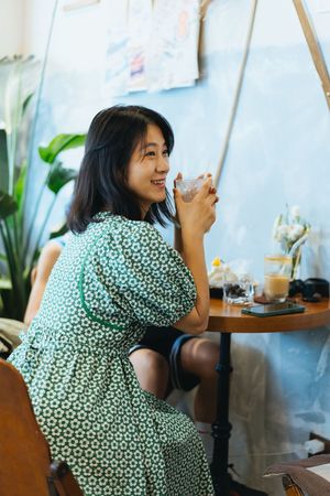 一位穿着连衣裙的女士坐在桌子前 面前放着一杯茶和一杯饮料 微笑着一个坐在咖啡馆的女孩。