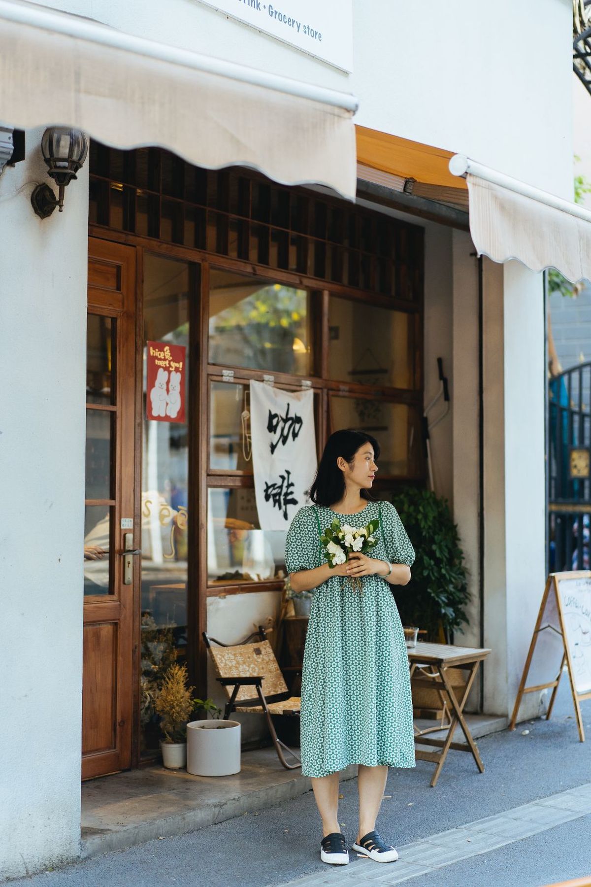 一位穿着绿色连衣裙的女子抱着花走在街上 花店在她面前。