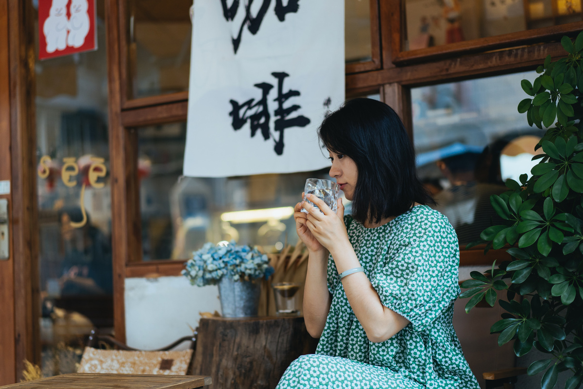 一位穿着绿色连衣裙的年轻女子坐在餐厅的桌子旁 喝着一杯酒。
