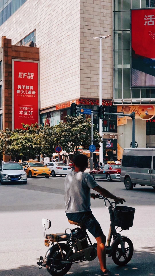 一名男子骑着轻便摩托车 提着篮子在一栋楼前的街道上行驶