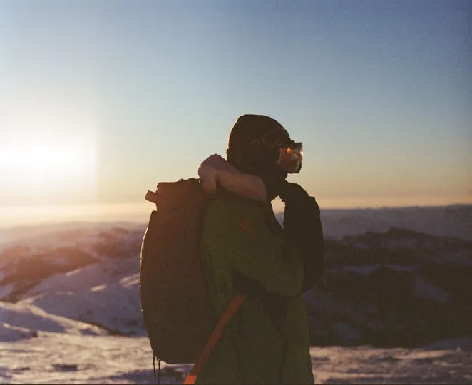 一个背着背包的男人拿着相机 拍下了一座被雪覆盖的山上日落的美景。