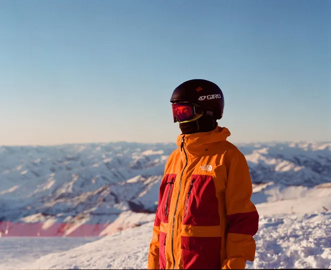 一个穿着橙色夹克和头盔站在雪山的男人