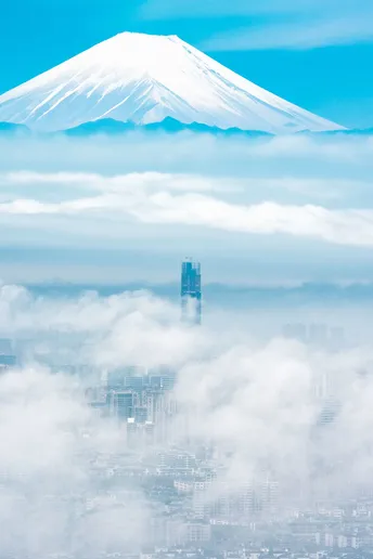 前景有高大的建筑 远处有被云层遮住的 mountains 上方有 clear blue sky。