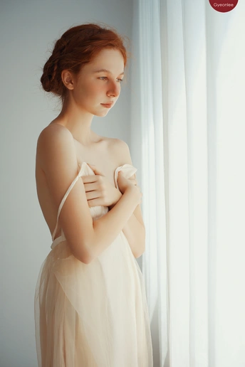 一位美丽的年轻女子穿着白色连衣裙站在窗户附近