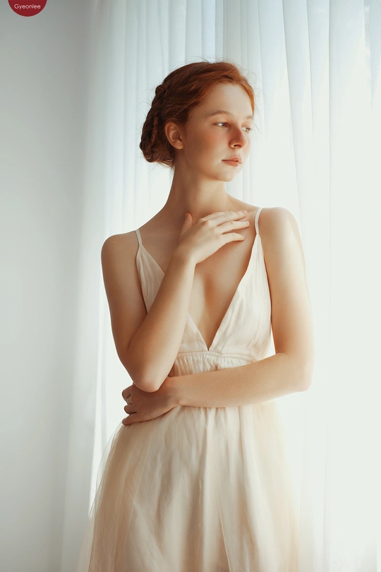 一位美丽的年轻女子穿着白色连衣裙 站在窗前 窗帘为薄纱。