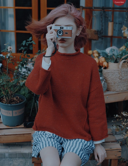 一位红发女青年坐在长凳上 用相机拍照。