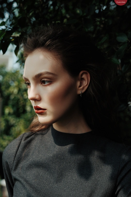 一位穿着全黑衣服的年轻女子在背景中有树木的肖像中摆姿势