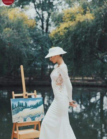 一位戴白色连衣裙和帽子的女士持有画有一名穿白色连衣裙的女子站在池塘前的画和另一幅画。