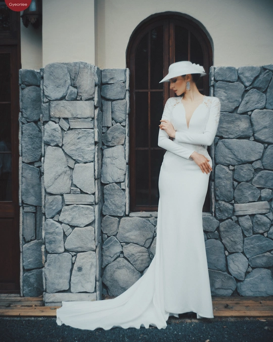 一位穿着白色连衣裙和帽子站在石头建筑前 有石头墙