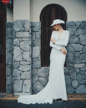 一位穿着白色连衣裙和帽子站在石头建筑前 有石头墙