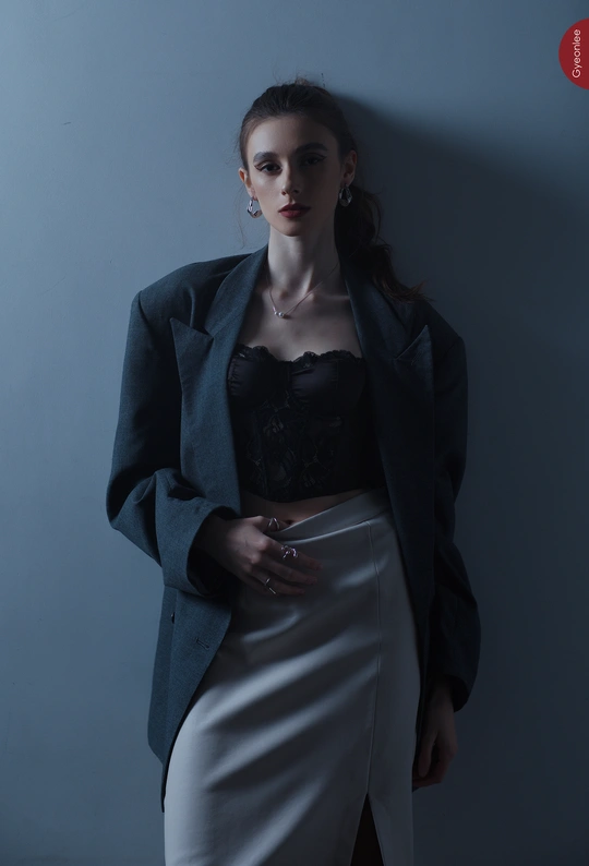 一位穿着黑色上衣和蓝色裙子的年轻女子站在蓝色墙壁前