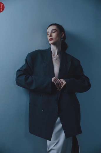 一位穿着黑色外套的女性站在蓝色墙壁前