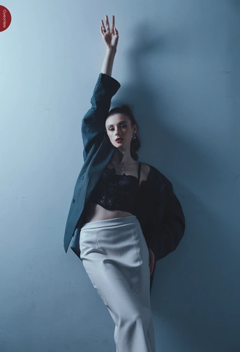 一位穿着蓝色夹克和白色裤子的女人站在墙边 双手举过头顶。