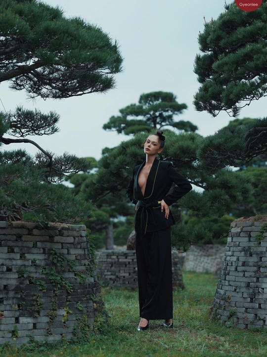 一位穿着黑色连衣裙的女士站在一个有石墙和松树苗的田地里