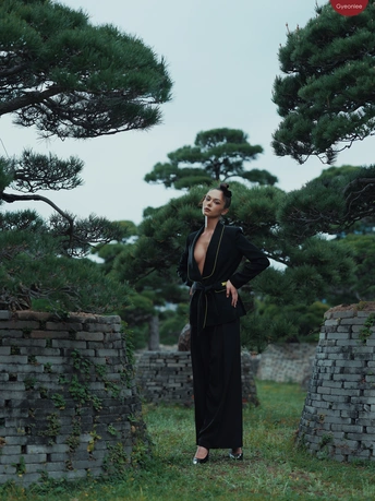 一位穿着黑色连衣裙的女士站在一个有石墙和松树苗的田地里