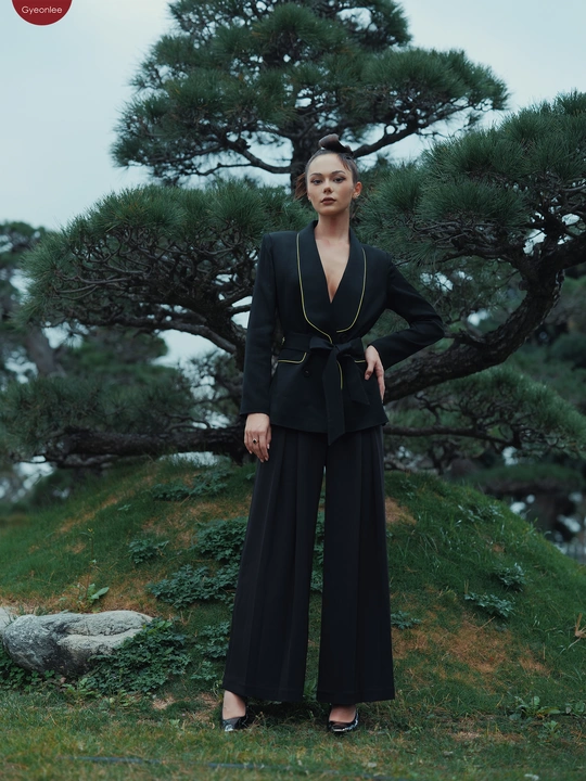 一个穿着黑色西装的模特站在一个山丘上 背景有一棵松树。