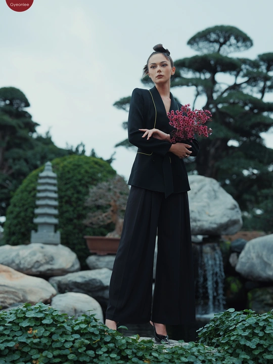 一位穿着全黑衣服的模特在瀑布和植物旁的花园中摆姿势