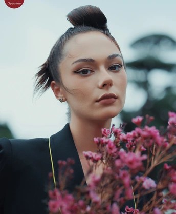 一位穿着全黑衣服的女士抱着紫色的花 背景有一位站着的人。