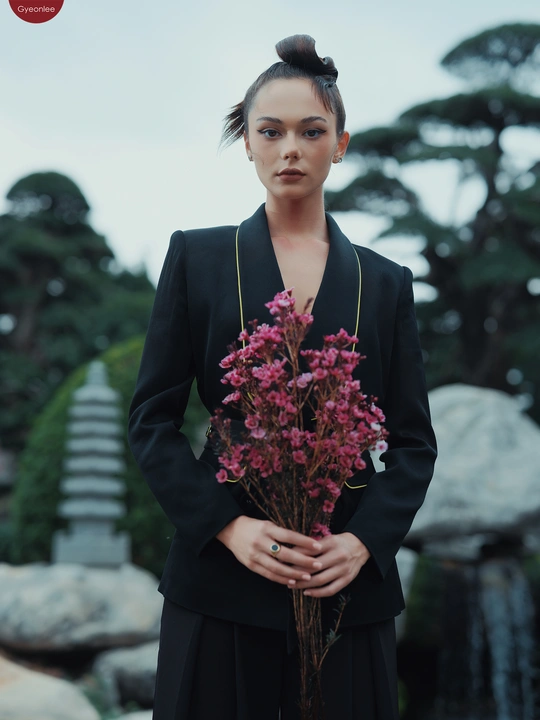 一位穿着黑色连衣裙的模特手拿一束紫花站在瀑布前