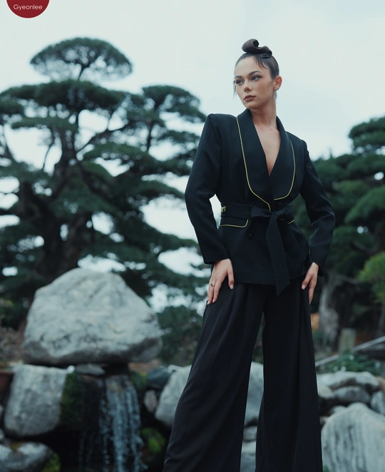 一个穿着黑色西装和裤子的模特站在瀑布和岩石前