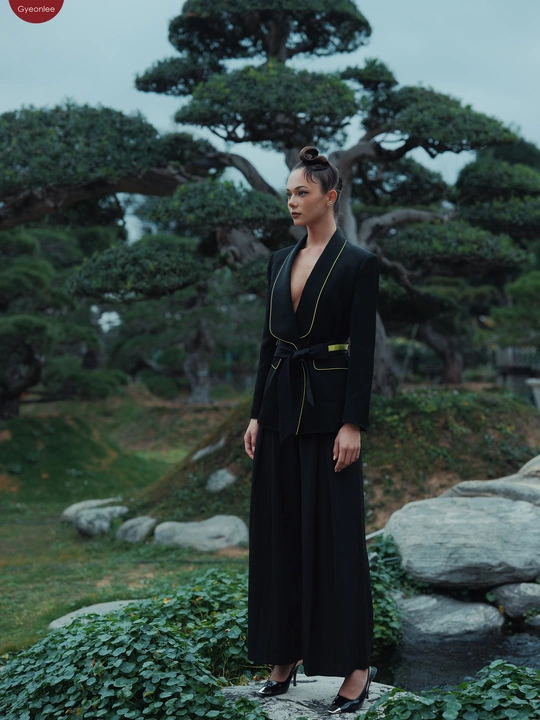 穿黑色连衣裙的模特站在岩石上 背景是花园里有树。