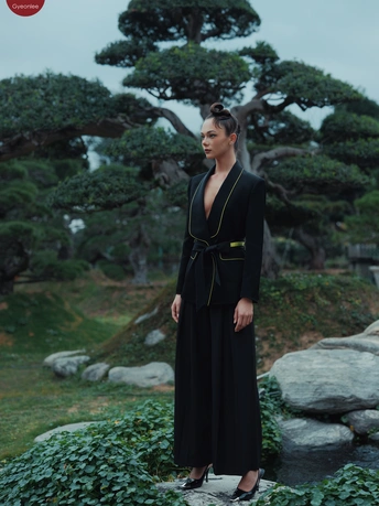 穿黑色连衣裙的模特站在岩石上 背景是花园里有树。