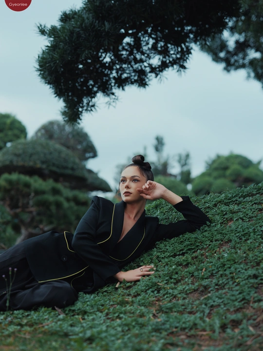 一位穿着黑色连衣裙的女人在绿山上与树木和草地一起摆姿势