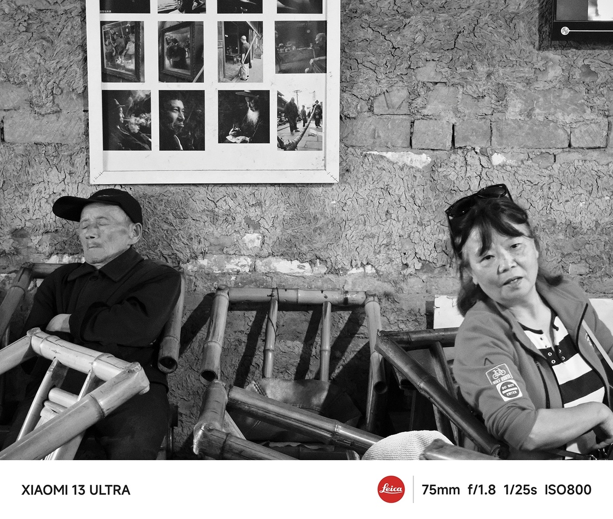 黑白色照片 一对男女坐在老建筑墙前的一排椅子上。
