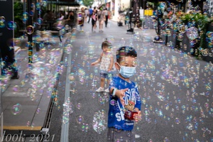 一个戴着面具的小男孩在街上漂浮的泡泡里玩耍