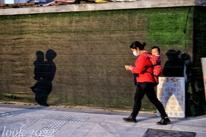 一名身穿红色夹克、戴着口罩的女子走在人行道上看手机