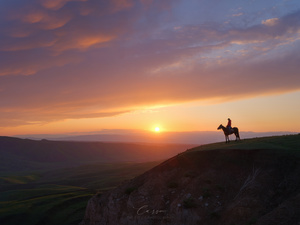 夕阳西下时 一个男子骑马在山坡上的剪影。