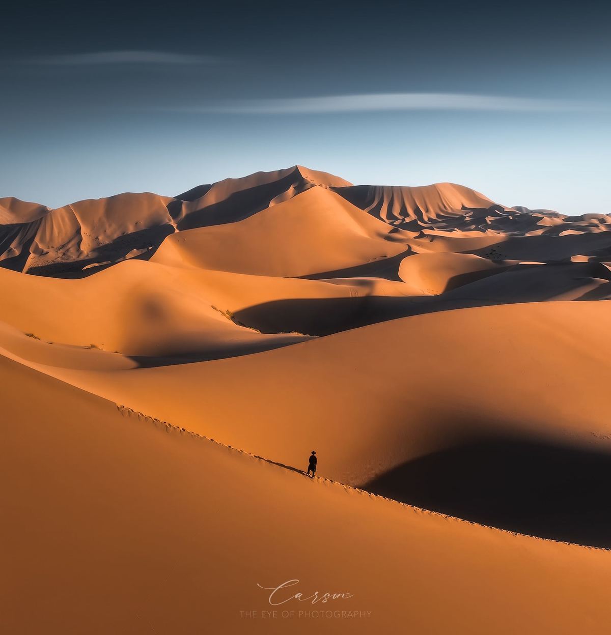 一个人站在沙漠中的大沙丘顶部 远处有山脉。