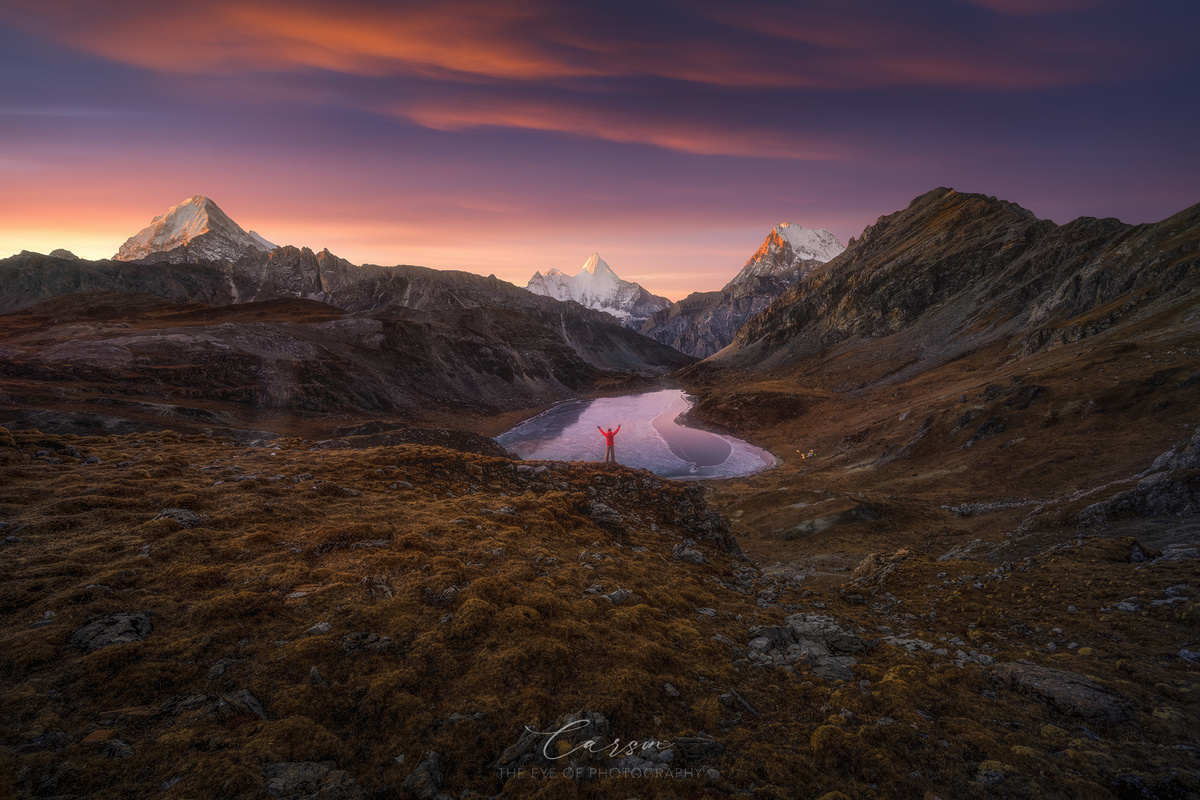 一个人穿着红衣服站在山中的湖边