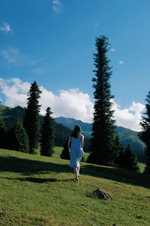 一位穿着白色连衣裙的年轻女子穿过山丘上的草地