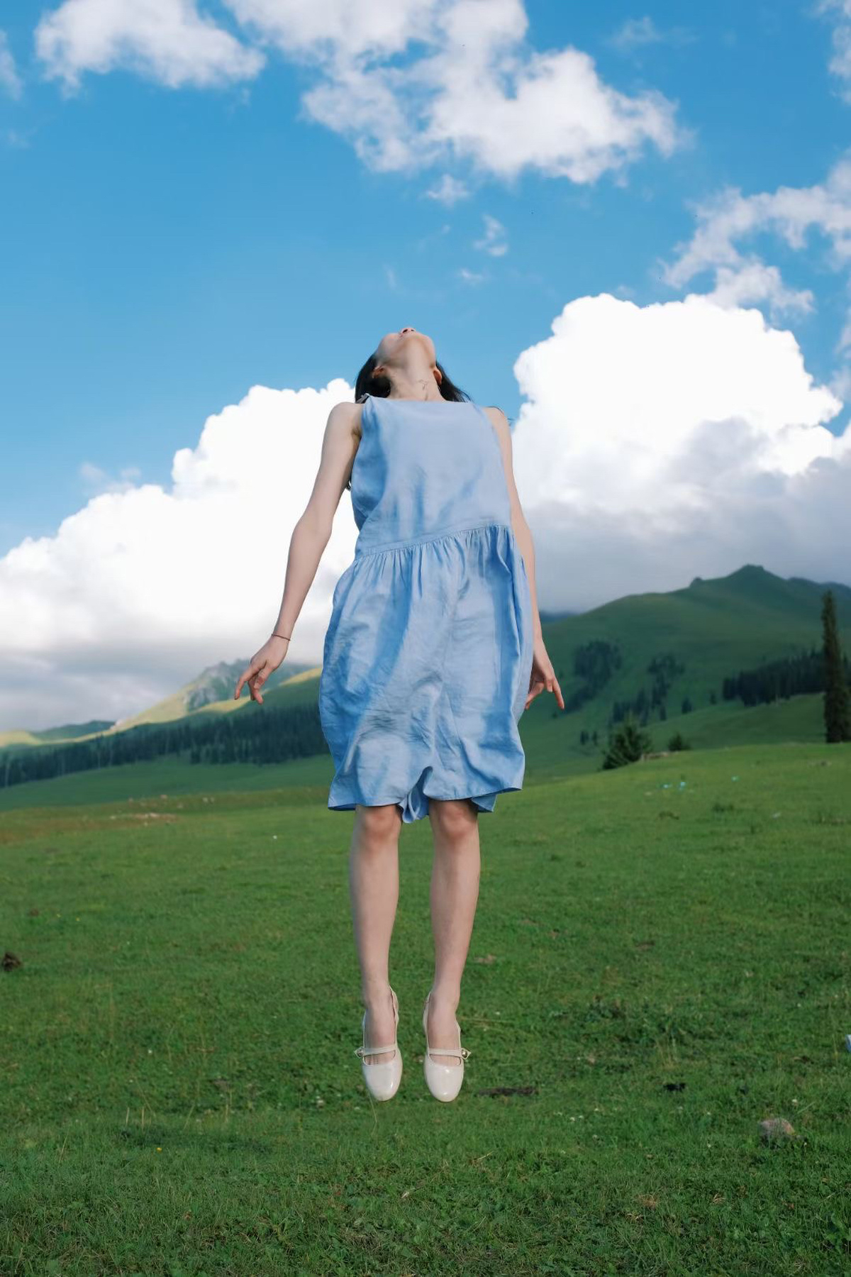 一位穿着蓝色连衣裙的年轻女子正在一片绿色的草地上行走 背景是山脉。