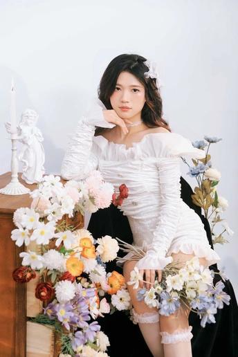 一个穿着白色连衣裙的年轻女子坐在花上