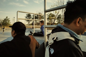 一个年轻男子站在滑板公园旁边 其他人正在观看 手里拿着滑板。