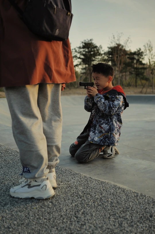 一位年轻男子站在滑板旁边 用相机给一个小男孩拍照。