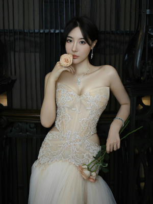 一位穿着白色连衣裙的年轻女子抱着玫瑰花在铁艺大门前摆姿势