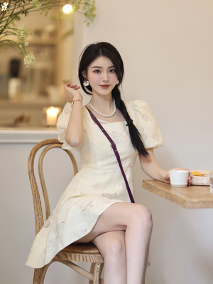 一个穿着白色连衣裙的年轻女子坐在桌子旁的一把椅子上 桌子上放着一个托盘 里面装着茶杯。