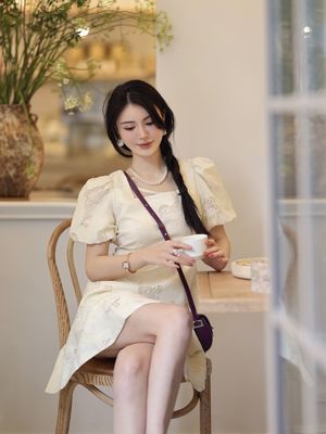 一个穿着白色连衣裙的年轻女子坐在椅子上 手里拿着一杯茶或咖啡。